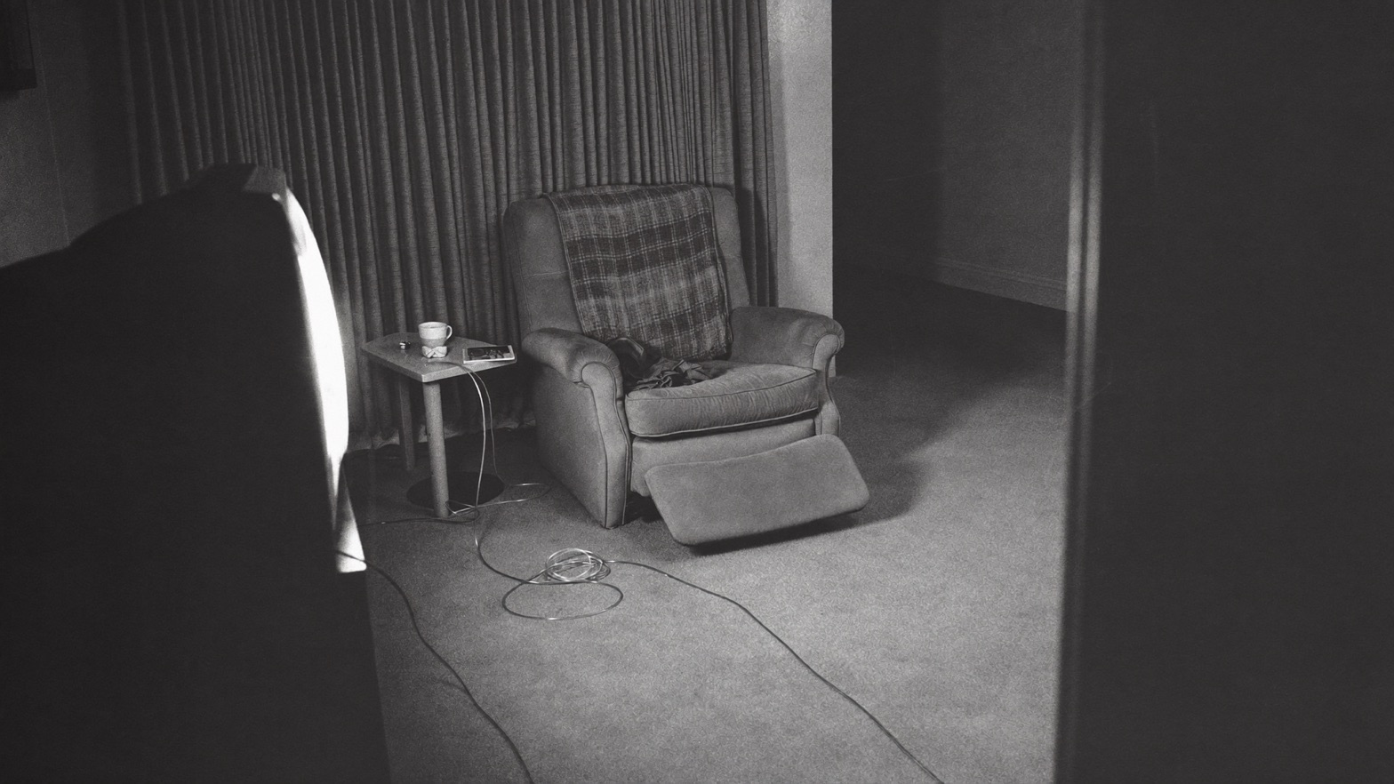 A quiet living room at night, lit by the television, oxygen tubing crossing the carpet